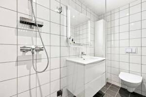 Badet har blant annet flislagte gulv og vegger, behagelig gulvvarme, innfelte downlights i himlingen, vegghengt toalett med innebygget sisterne og dusjsone med glassvegg.
